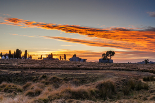 Silhouette of farmyard buildings under a sunrise sky - Australian Stock Image