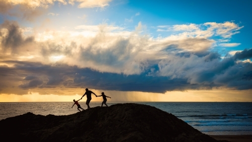 Silhouette of father and sons walking together holding hands on sand dune - Australian Stock Image