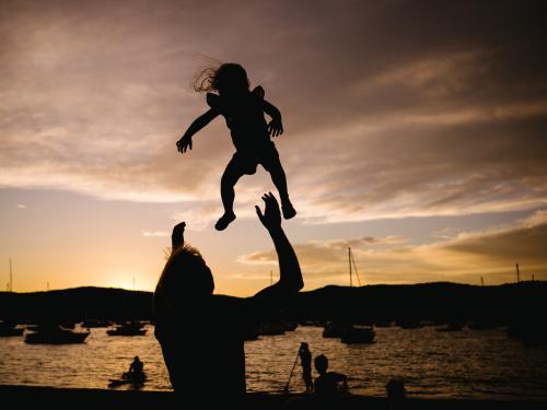 Silhouette of father throwing daughter into the air at sunset