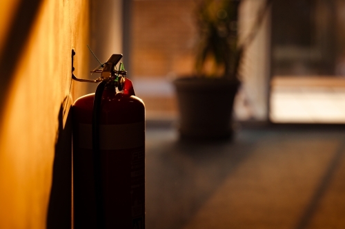 Silhouette of fire extinguisher in motel hallway illuminated by golden afternoon sunlight - Australian Stock Image