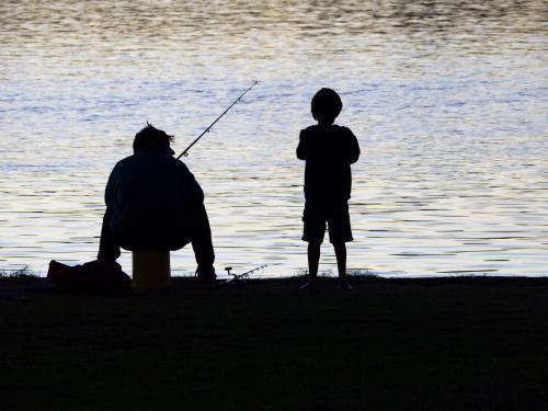Silhouette of fisherman and boy at water's edge - Australian Stock Image
