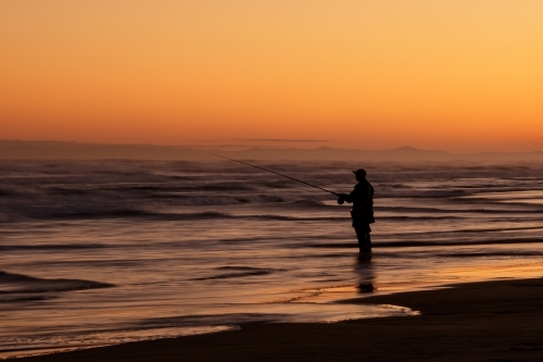 Silhouette of fisherman standing in shallow water at sunset