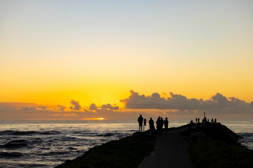 Silhouette of group of people gathering to watch the sunrise from the breakwall at Brunswick Heads - Australian Stock Image