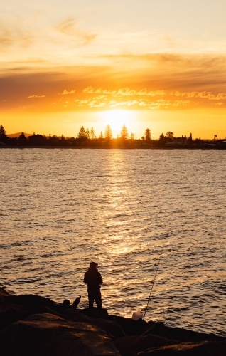 Silhouette of man fishing at sunset from the breakwall at Stockton, NSW - Australian Stock Image