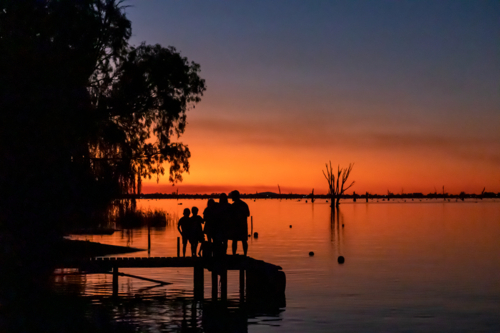 Silhouette of people on jetty with sunset over lake - Australian Stock Image