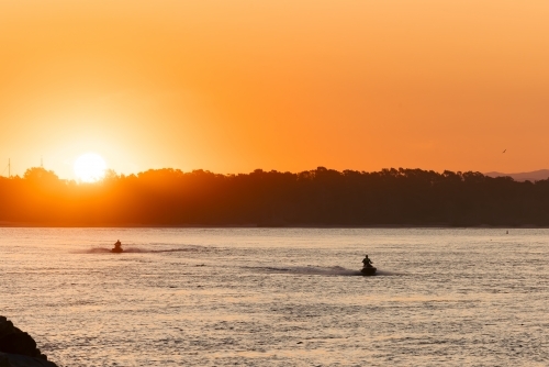 Silhouette of people riding jet skis across the bay at Port Macquarie at sunset - Australian Stock Image
