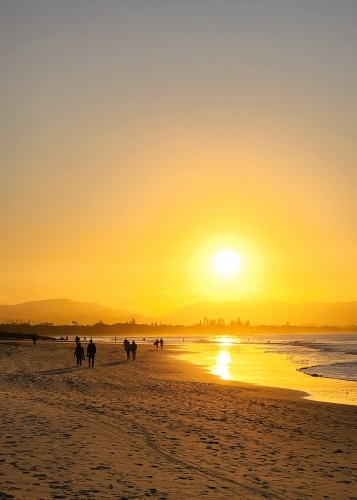 Silhouette of people walking on the beach at Byron Bay at sunset - Australian Stock Image