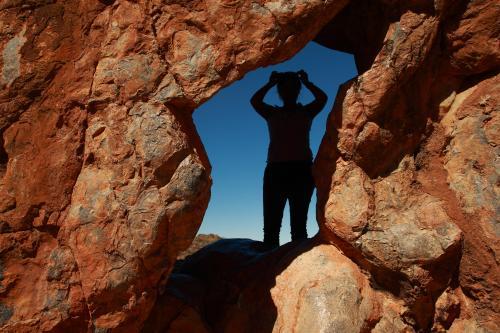 Silhouette of person inside a hole in red rock - Australian Stock Image