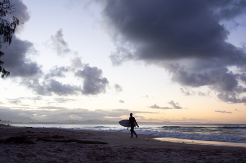 Silhouette of surfer leaving the beach as dusk - Australian Stock Image