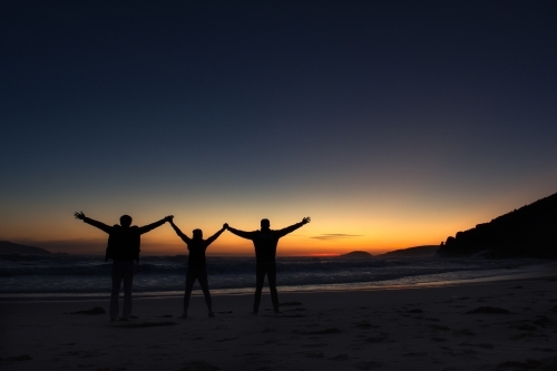 Silhouette of three friends holding hands raising against a sunset background