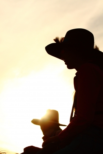 Silhouette of two country girls in their twenties, as they ride their horses - Australian Stock Image