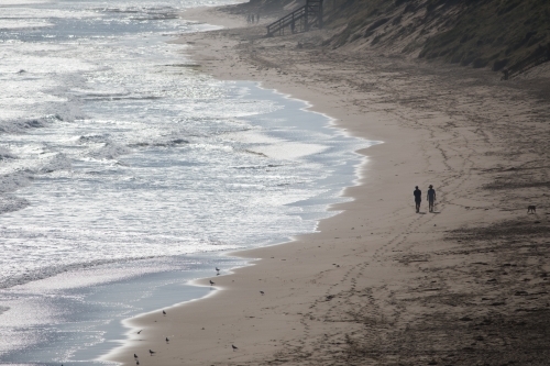 Silhouette of two distant people walking along a beach - Australian Stock Image