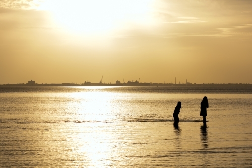Silhouette of two people standing knee-deep in still water at sunset