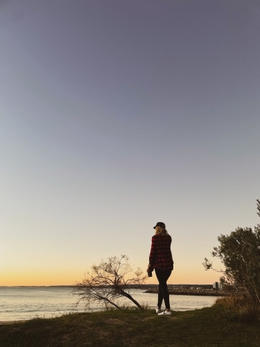 Silhouette of woman standing in front of coastal marina background at twilight - Australian Stock Image