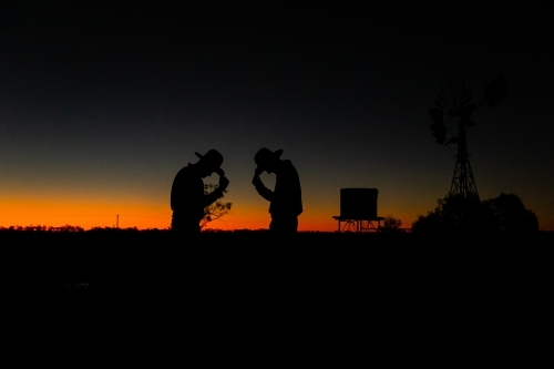 Silhouette shot of two men wearing hats looking down during sunset - Australian Stock Image