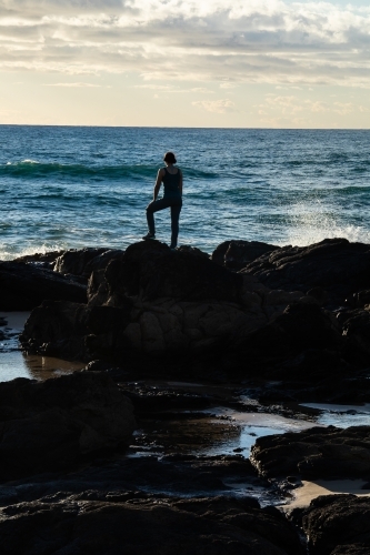 Silhouetted female standing on rocky headland early in the morning - Australian Stock Image