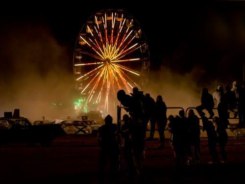Silhouetted spectators watching a demolition derby with ferris wheel - Australian Stock Image