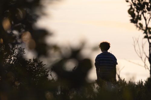 Silhouetted teenage woman looking at sunset view of calm sea while bush walking in nature - Australian Stock Image