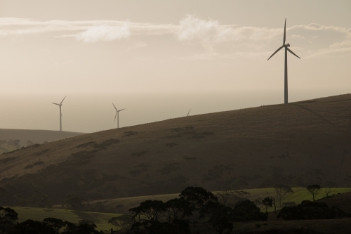 Silhouetted wind turbines on a hill in a paddock - Australian Stock Image