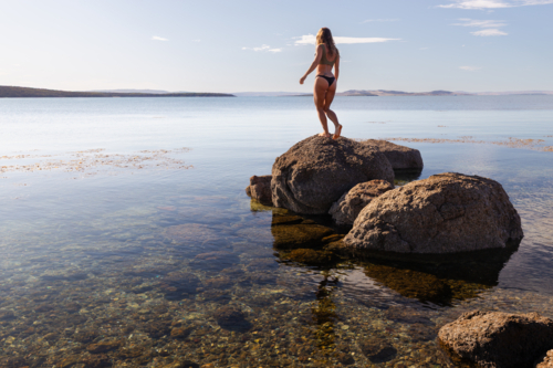 Silhouetted woman in bikini exploring calm coastline during summer in South Australia - Australian Stock Image