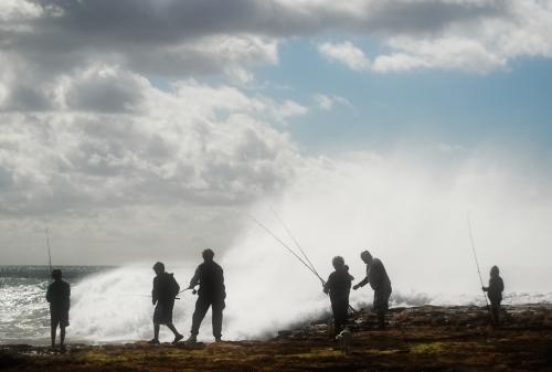Silhouettes of people fishing off the beach with big waves