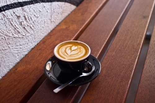 Single flat white coffee sitting on a wooden table - Australian Stock Image