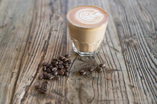 Single latte sitting on a wooden table with scattered coffee beans - Australian Stock Image
