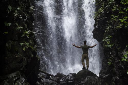 Single man with arms lifted in front of waterfall - Australian Stock Image