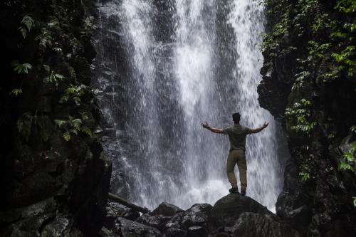 Single man with arms lifted in front of waterfall