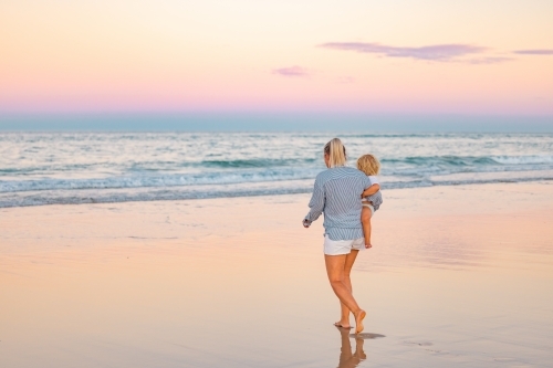 Single mother carrying son on the beach in twilight light. Sunset on the Gold Coast - Australian Stock Image