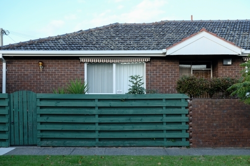 Single storey brick house with green fence - Australian Stock Image