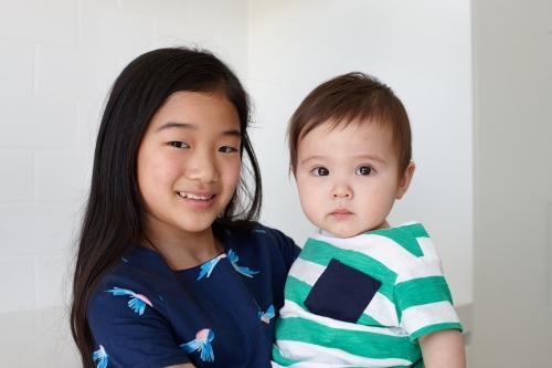 Sister holding younger baby brother in kitchen - Australian Stock Image