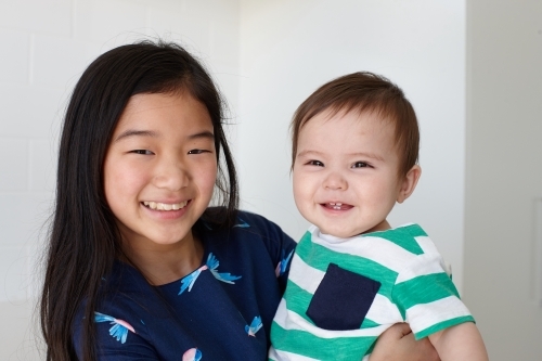 Sister holding younger baby brother in kitchen - Australian Stock Image