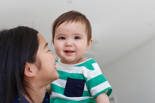 Sister holding younger baby brother in kitchen - Australian Stock Image