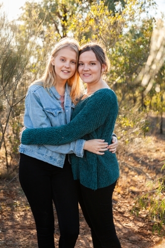 Sisters laughing together and giving one another a hug - Australian Stock Image