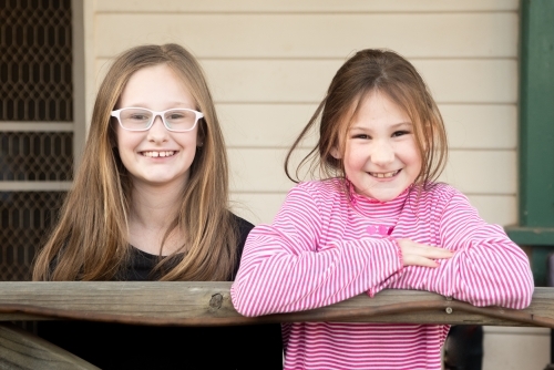 Sisters standing on the veranda of their house. - Australian Stock Image