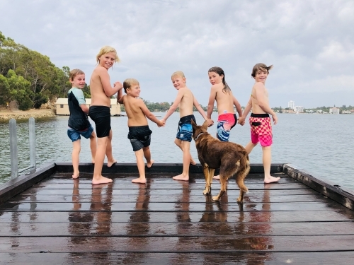 Six kids holding hands smiling at camera, about to jump of a pier