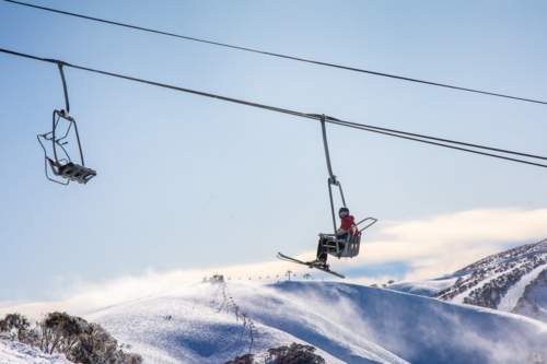 Skier on chairlift with mountain in background on a sunny day - Australian Stock Image