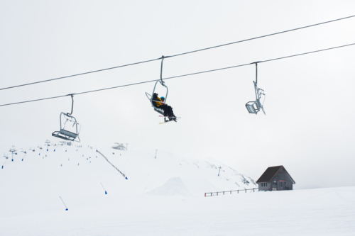 Skiers on ski lift with cabin and snowy mountain in background - Australian Stock Image