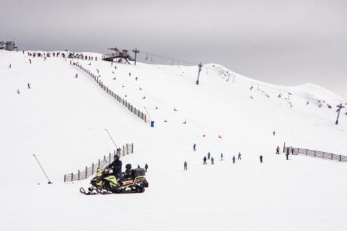 Skiiers on mountain with ski lift and race course, with ski-doo in foreground Mt Buller, Victoria - Australian Stock Image