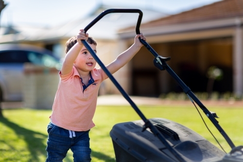 Small child trying to push lawnmower - Australian Stock Image