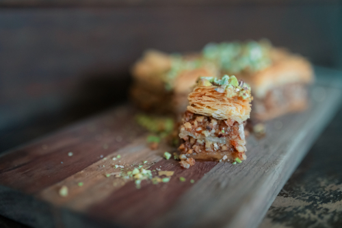 Small piece of Baklava traditional pastry dessert on wooden board with chopped pistachios - Australian Stock Image