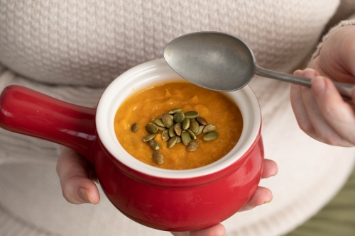 small red bowl of pumpkin soup in lady's hands with pepitas