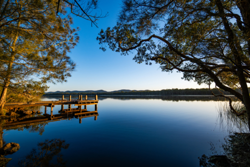 Small timber jetty at sunrise beside calm water - Australian Stock Image