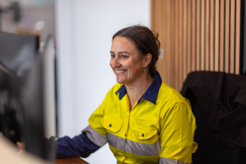 smiling adult woman in high visibility clothes working in front of her computer in an office. - Australian Stock Image