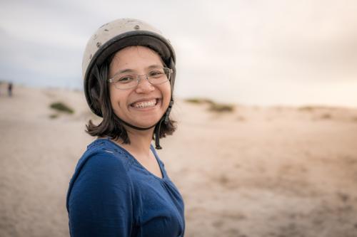 Smiling Asian mother ready to ride camels on beach at sunset