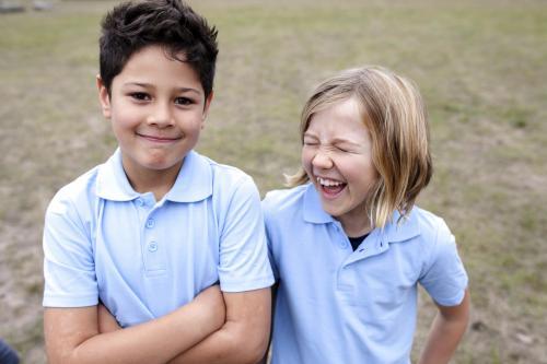 Smiling boy and girl standing outside wearing school unifom - Australian Stock Image
