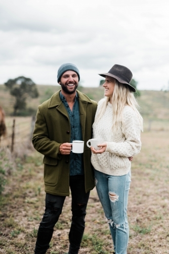 Smiling couple on farm holding coffee cups - Australian Stock Image