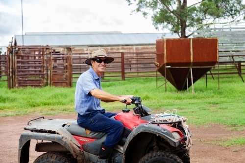 Smiling farmer on quad bike with hat and sunglasses - Australian Stock Image