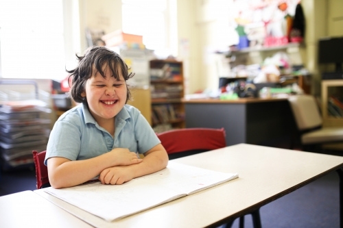 smiling girl wearing a pale blue shirt with short hair sitting on a table with a drawing pad - Australian Stock Image